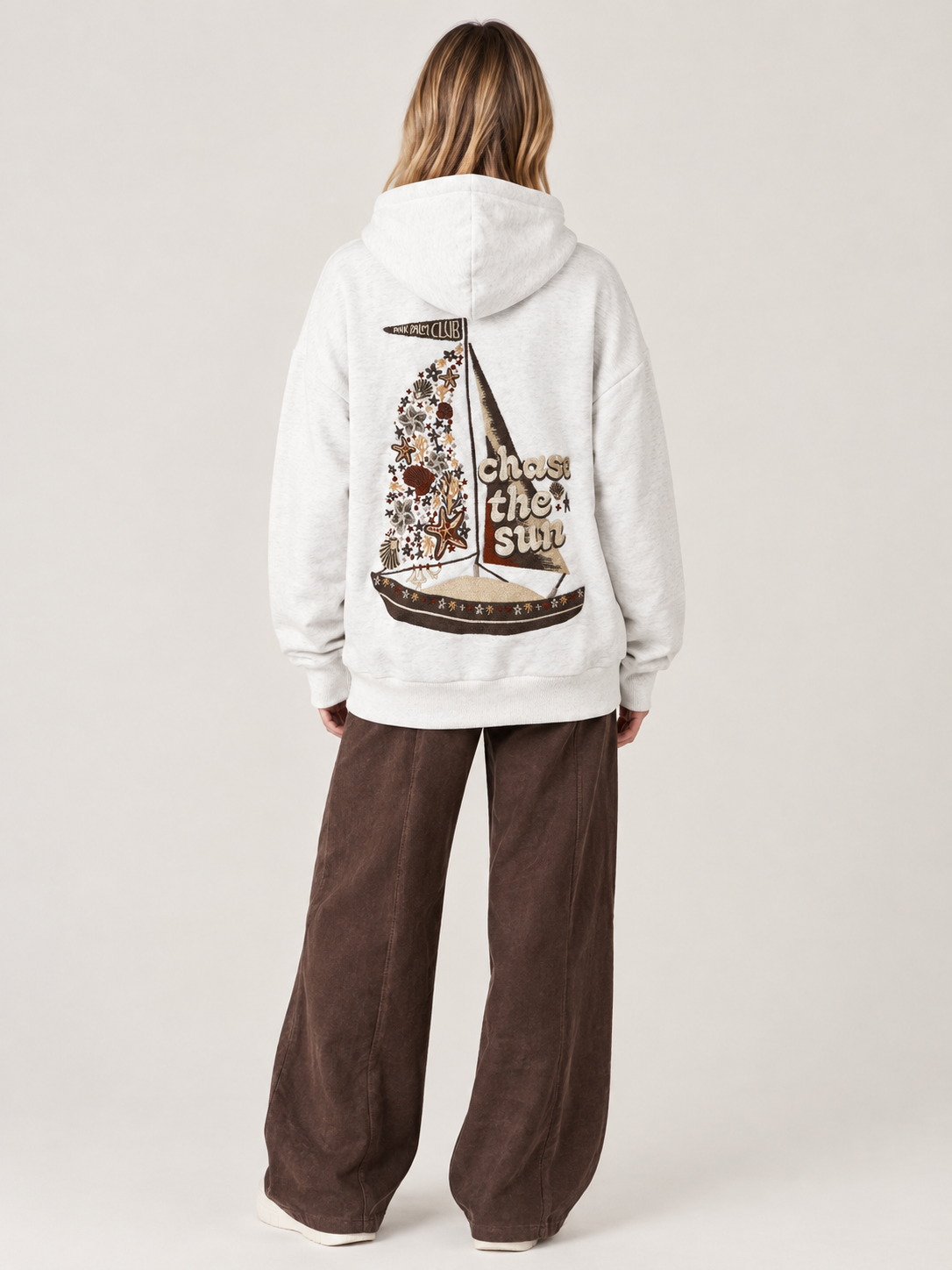White oversized hoodie with a brown boat design on the back and writing on the front.