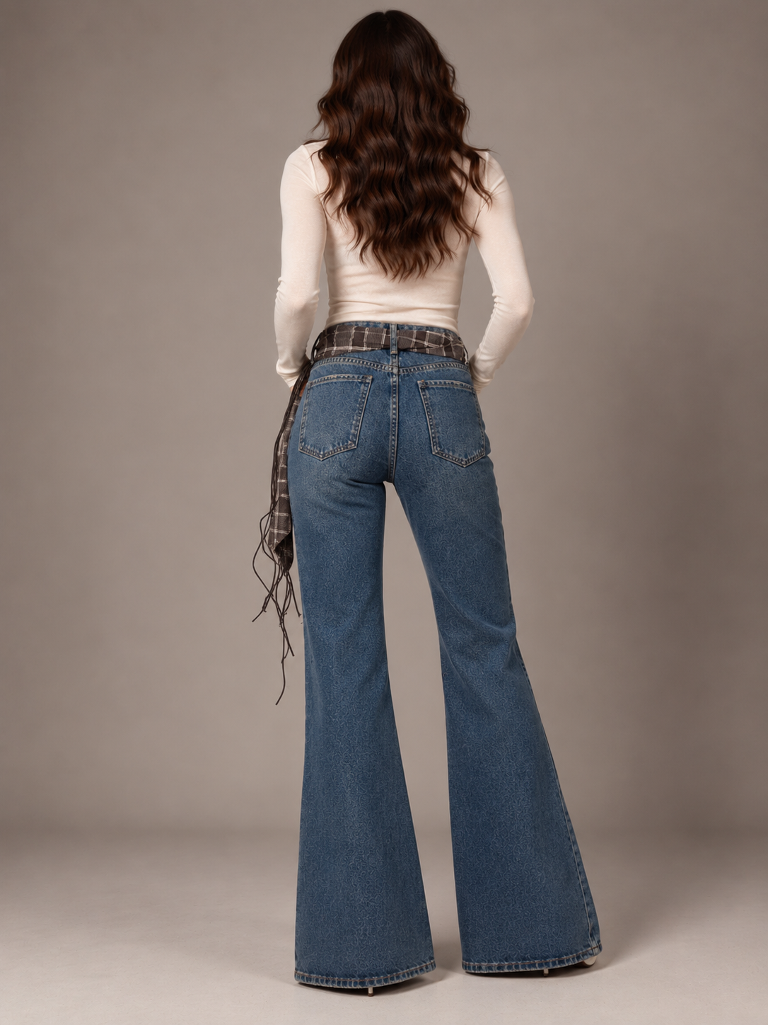 Blue flared jeans with a brown plaid belt featuring fringe.